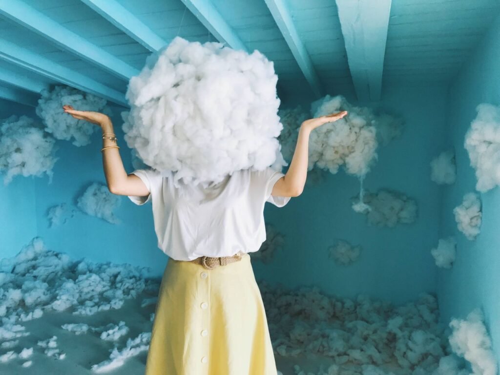 Whimsical art piece with a person having a cloud as a head in a blue room filled with clouds.